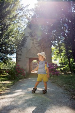 Küçük, güzel bir evin önünde duran bir çocuk, arkasında ışık huzmeleri.