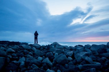 Kayalıklarda dikilip İzlanda 'da gün batımını izleyen bir adamın silueti.