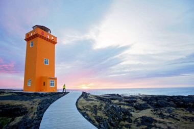 Çocuklar, gün batımında İzlanda 'daki Snaefellsjokull Ulusal Parkı' nda, lav tarlasında deniz fenerine doğru koşuyorlar.