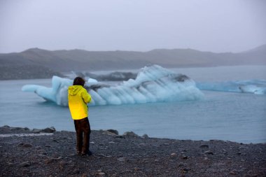 Çocuk, yağmurlu bir günde akşam erken saatlerde İzlanda 'daki buzdağı gölünde fotoğraf çekiyor. 