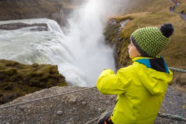 Çocuklar, İzlanda 'daki dağlardaki görkemli Gullfoss şelalesinin tadını çıkarıyorlar.