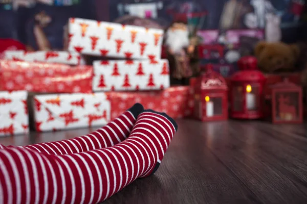 足の再生にクリスマスソックスを着て 子供の贈り物の前に座っている 家でリラックスしてる — ストック写真