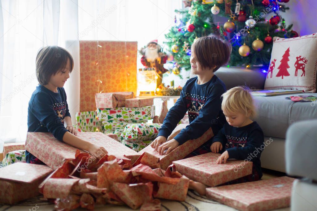 Happy children, boys, opening presents on christmas day, dressed in pajamas
