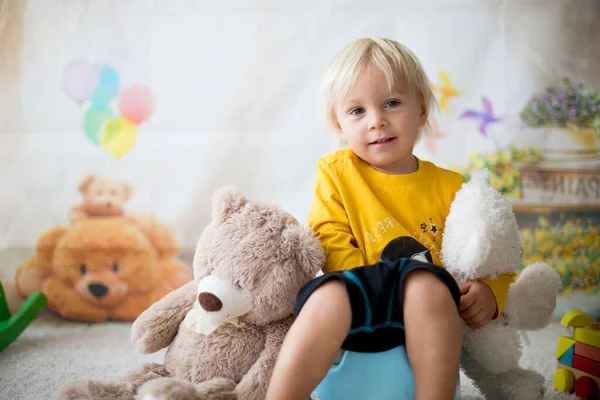 Cute toddler boy, potty training, playing with his teddy bear on potty