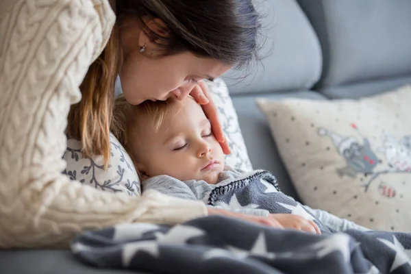 熱のある部屋のソファの上に寝そべってる子供は病気で母親は体温をチェックして家で休んでる — ストック写真