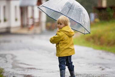 Şirin sarışın çocuk, evlat, kırsal bir yolda sisli bir sonbahar gününde yağmurda şemsiyeyle oynuyor.