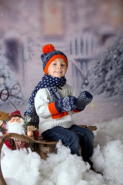 Kış kıyafetli, karda oynayan, Noel stüdyosu fotoğrafı çeken tatlı bir çocuk.