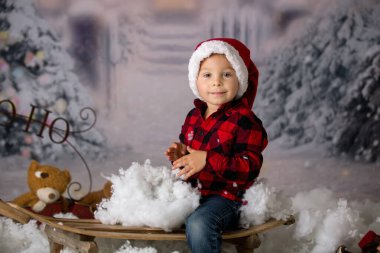 Kış kıyafetli, karda oynayan, Noel stüdyosu fotoğrafı çeken tatlı bir çocuk.
