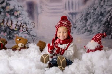 Kış kıyafetli, karda oynayan, Noel stüdyosu fotoğrafı çeken tatlı bir çocuk.