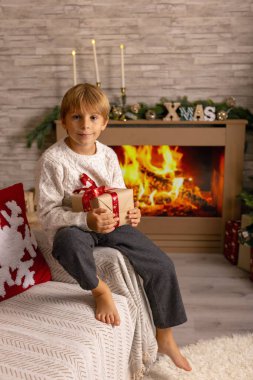 Sevimli anaokulu çocuğu, şöminenin önünde oturuyor, Noel hediyesini tutuyor ve evde kitap, eğlence ve mutluluk okuyor.