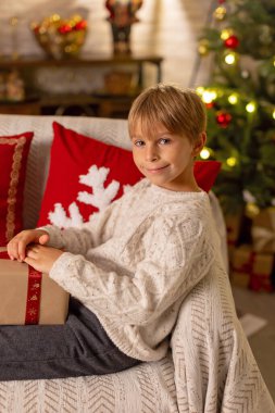 Sevimli anaokulu çocuğu, şöminenin önünde oturuyor, Noel hediyesini tutuyor ve evde kitap, eğlence ve mutluluk okuyor.