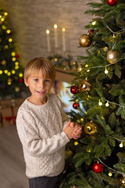 Sevimli anaokulu çocuğu, şöminenin önünde oturuyor, Noel hediyesini tutuyor ve evde kitap, eğlence ve mutluluk okuyor.