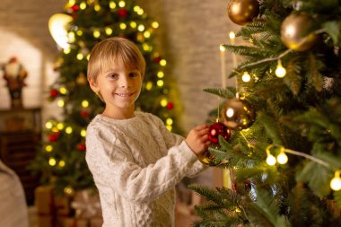 Sevimli anaokulu çocuğu, şöminenin önünde oturuyor, Noel hediyesini tutuyor ve evde kitap, eğlence ve mutluluk okuyor.
