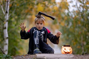 Cadılar Bayramı kostümlü bir ormanda çocuk, mumlarla ve dekorasyonla oyulmuş balkabakları, ürkütücü konsept, Cadılar Bayramı teması