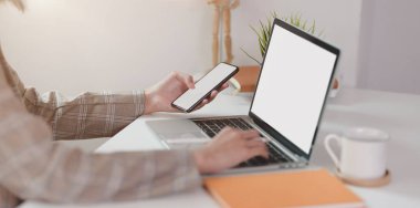 Akıllı telefonu tutarken dizüstü bilgisayarda yazan iş kadını 