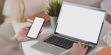 Akıllı telefonu tutarken dizüstü bilgisayarda yazan genç iş kadını