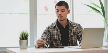 Dizüstü bilgisayar kullanırken projesi üzerinde çalışan genç erkek tasarımcı 