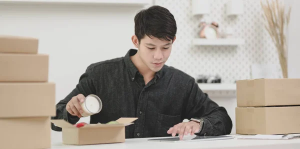 Joven dueño de una pequeña empresa masculina comprobando los pedidos y preparando el producto — Foto de Stock