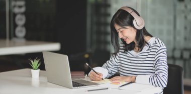 Müzik dinlerken fikrini not defterine yazarak projesi üzerinde çalışan kadın serbest çalışan 