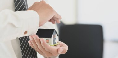 Elinde bir ev modeli tutan sigorta acentesi, ev sigortası sembolü