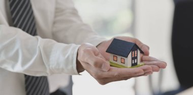 Elinde bir ev modeli tutan sigorta acentesi, ev sigortası sembolü