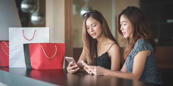 Deux belles femmes asiatiques vérifiant leur smartphone et bavardant ensemble après avoir fait du shopping dans le centre commercial — Photo