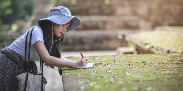 Fiatal ázsiai lány jegyzetel a régi templom látogatása közben az ókori történelmi helyek az ünnep során — Stock Fotó