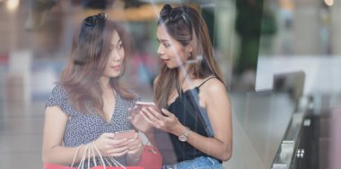İki Asyalı kadın birlikte sohbet ve alışveriş merkezinde alışveriş yaparken akıllı telefon tutarak 