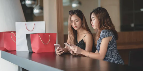 Две красивые азиатки проверяют свой смартфон и общаются после покупки в торговом центре. — стоковое фото