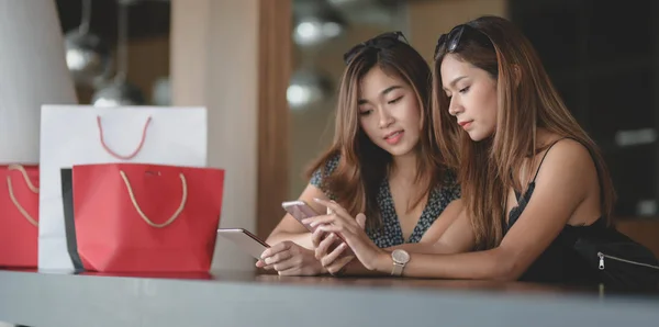 Deux belles femmes asiatiques vérifiant leur smartphone et bavardant ensemble après avoir fait du shopping dans le centre commercial — Photo