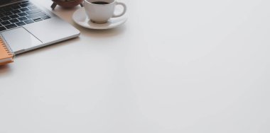 Kopyalama alanı ile beyaz ahşap masa üzerinde dizüstü bilgisayar, kahve fincanı ve ofis malzemeleri ile minimal işyeri 