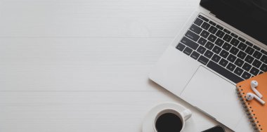 Beyaz ahşap masa üzerinde dizüstü bilgisayar, kahve fincanı ve ofis malzemeleri ile minimal işyeri üst görünümü 