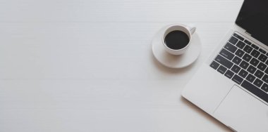 Dizüstü bilgisayar ve beyaz ahşap masa üzerinde bir fincan kahve ile minimal işyeri üst görünümü 