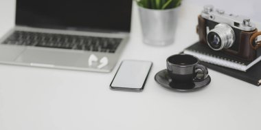 Beyaz masa üzerinde dizüstü bilgisayar, akıllı telefon ve ofis malzemeleri ile modern fotoğrafçı işyeri 