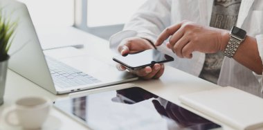 Modern ofiste, projelerini hazırlarken akıllı telefonuna dokunan genç adamın yakın plan görüntüsü. 