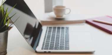 Açık dizüstü bilgisayarı, kahve fincanı ve ofis malzemeleri olan rahat bir iş yeri. 