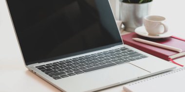 Açık dizüstü bilgisayarı, kahve fincanı ve ofis malzemeleri olan modern rahat iş yeri.