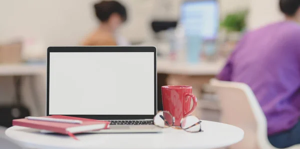 Blanco scherm laptop computer met kantoorbenodigdheden in modern kantoor en zakenvrouwen op de achtergrond — Stockfoto
