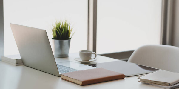 Modern workplace next to the windows with laptop computer, table and office supplies on white wooden desk 