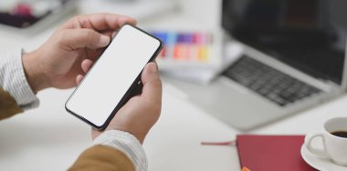 Boş ekranlı akıllı telefonu kırtasiyeli rahat bir iş yerinde tutan genç adam, okul kavramlarına geri dönüyor.