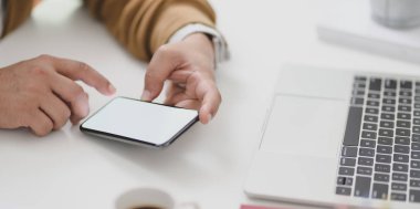 Genç işadamı dizüstü bilgisayarla projesi üzerinde çalışırken boş ekran akıllı telefonuyla bilgiye bakıyor 