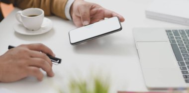 Genç işadamı boş ekran akıllı telefonuna bakarken projesinde çalışıyor.