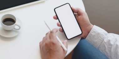 Genç profesyonel işadamı çalışma alanındaki boş ekranlı akıllı telefondan bilgi arıyor. 