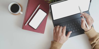Proje üzerinde çalışan genç adamın en iyi görüntüsü. Ofis malzemeleriyle rahat bir iş yerinde tabletle çalışıyor. 