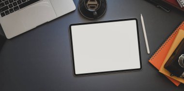 Karanlık ve modern iş yerinde dizüstü bilgisayar ve diğer ofis malzemeleriyle boş ekran tabletinin genel görüntüsü 