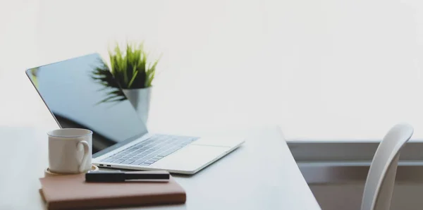 Laptop mit Kaffeetasse und Bürobedarf in komfortablem Arbeitsplatz in Fensternähe mit Dekorationen — Stockfoto