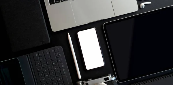 어두운 배경의 사무실 공급 장치가 있는 빈 화면 스마트폰 및 기타 전자 기기가 있는 어두운 트렌디 작업 공간의 상단 사진 — 스톡 사진
