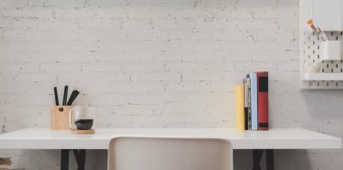 Ofis malzemeleri ve dekorasyonları beyaz ahşap masa arkaplanı ve beyaz tuğlalı duvar olan küçük bir ofis. 