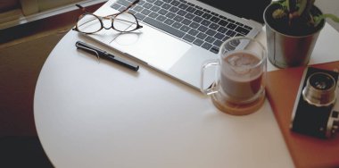 Dizüstü bilgisayarlı rahat bir iş yeri, sıcak kakao bardağı ve beyaz ahşap masadaki ofis malzemeleri. 