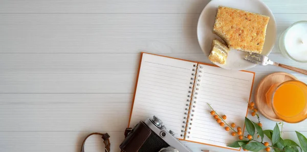 Overhead πλάνο του άνετο χώρο εργασίας με κενό σημειωματάριο με ψωμί τοστ και ένα ποτήρι χυμό πορτοκαλιού σε λευκό ξύλινο τραπέζι — Φωτογραφία Αρχείου